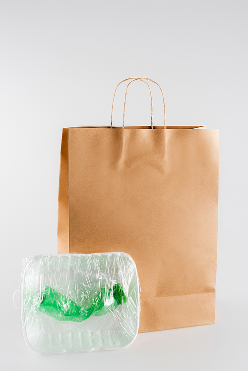 plastic plate and bottle packed in cellophane near paper bag on grey, ecology concept