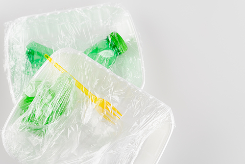 top view of plastic plates with fork and bottle packed in cellophane, ecology concept