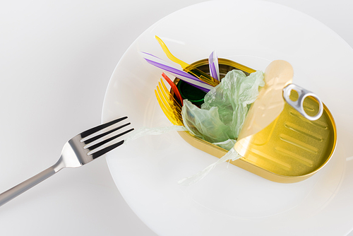 tin with polyethylene garbage on plate near fork on white, ecology concept