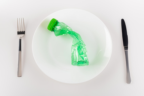 top view of plate with plastic bottle near knife and fork on white, ecology concept