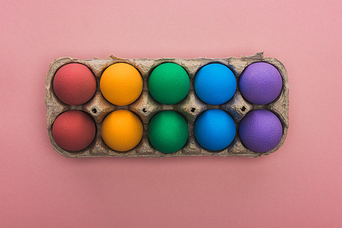 top view of painted Easter eggs in cardboard box on pink background