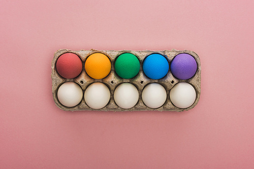 top view of painted Easter eggs in cardboard box on pink background