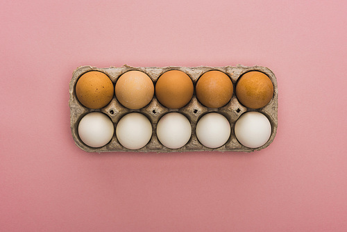 top view of chicken eggs in cardboard box on pink background