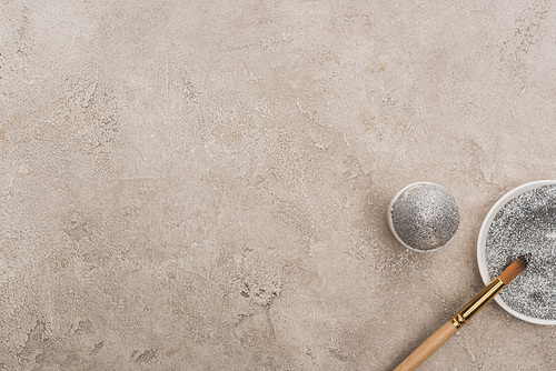 top view of chicken egg, silver glitter with paintbrush on grey concrete surface