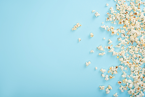 top view of scattered crispy popcorn on blue, cinema concept