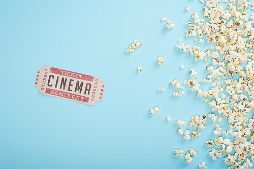top view of cinema ticket near scattered popcorn on blue
