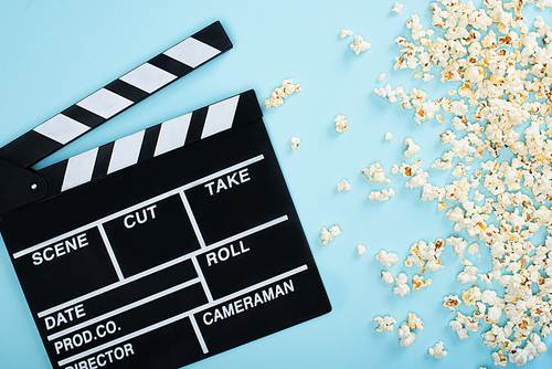 top view of clapperboard near popcorn scattered on blue, cinema concept