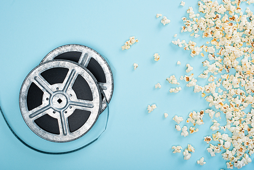 top view of film reels near scattered popcorn on blue, cinema concept