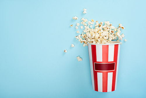top view of striped carton bucket with popcorn on blue, cinema concept