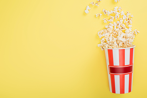 top view of striped bucket with crunchy popcorn on yellow, cinema concept