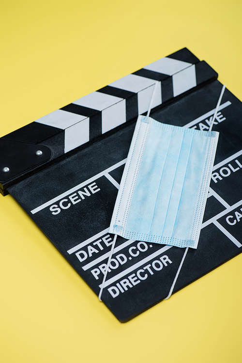 medical mask and clapper board on yellow, cinema concept