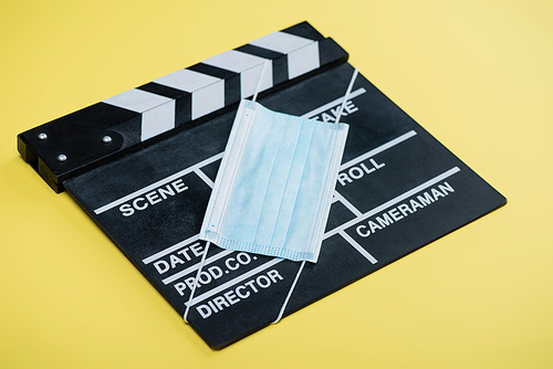medical mask on clapperboard on yellow, cinema concept