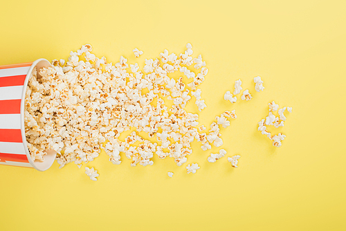 top view of paper bucket and scattered popcorn on yellow, cinema concept