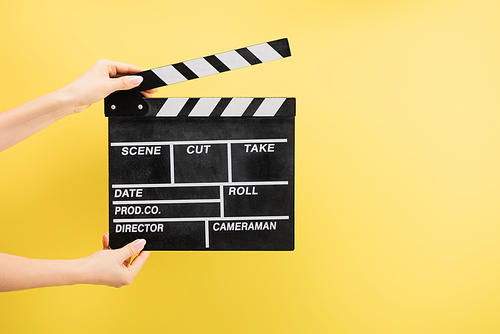 partial view of camera assistant holding clapperboard isolated on yellow, cinema concept