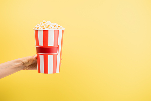 partial view of woman holding bucket of delicious popcorn isolated on yellow, cinema concept
