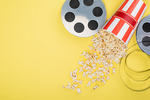 top view of film reels near bucket with scattered popcorn on yellow, cinema concept