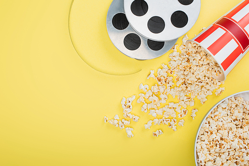 top view of film coils near buckets with popcorn on yellow, cinema concept