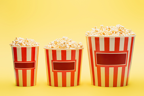 big, medium and small buckets of popcorn on yellow, cinema concept
