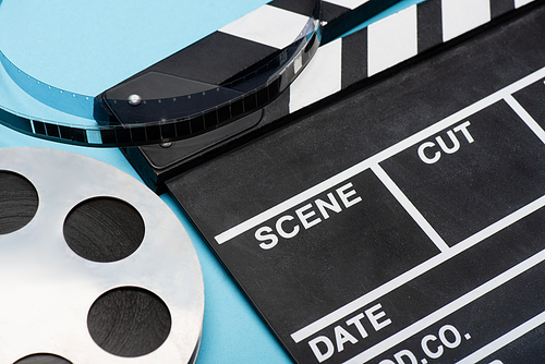 close up view of clapperboard and film bobbin on blue, cinema concept