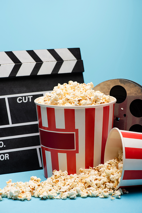 buckets of popcorn, clapperboard and film bobbin on blue, cinema concept