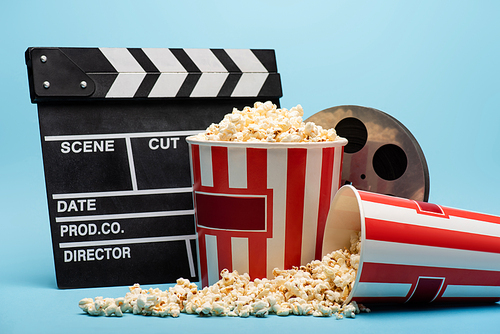 clapperboard, film reel and buckets with popcorn on blue, cinema concept
