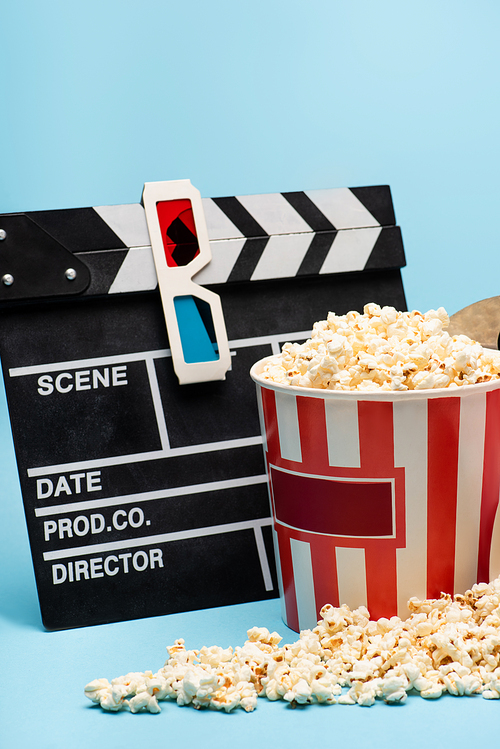 clapperboard, 3d glasses and bucket with tasty popcorn on blue, cinema concept