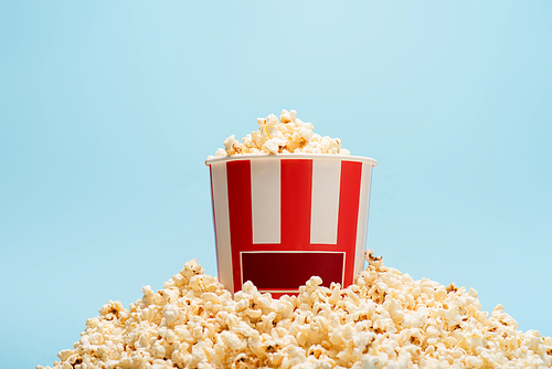 striped paper bucket with crunchy popcorn isolated on blue, cinema concept