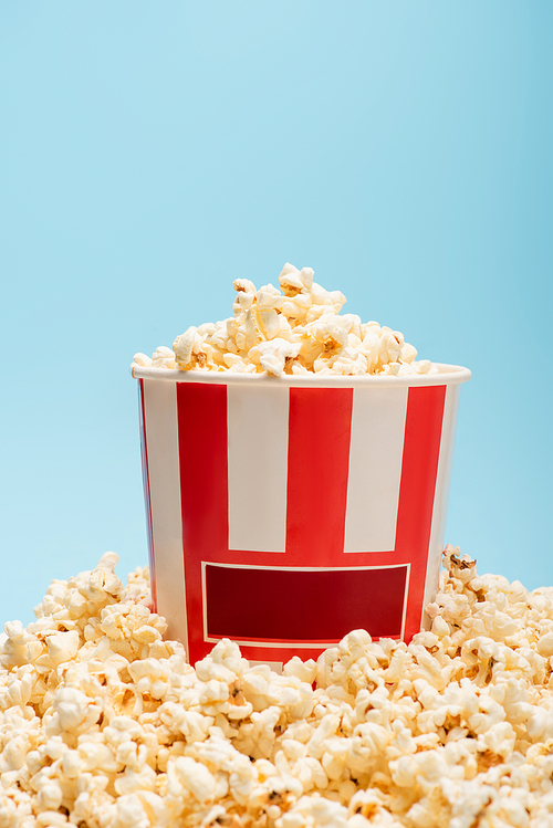 striped bucket and pile of tasty popcorn isolated on blue, cinema concept