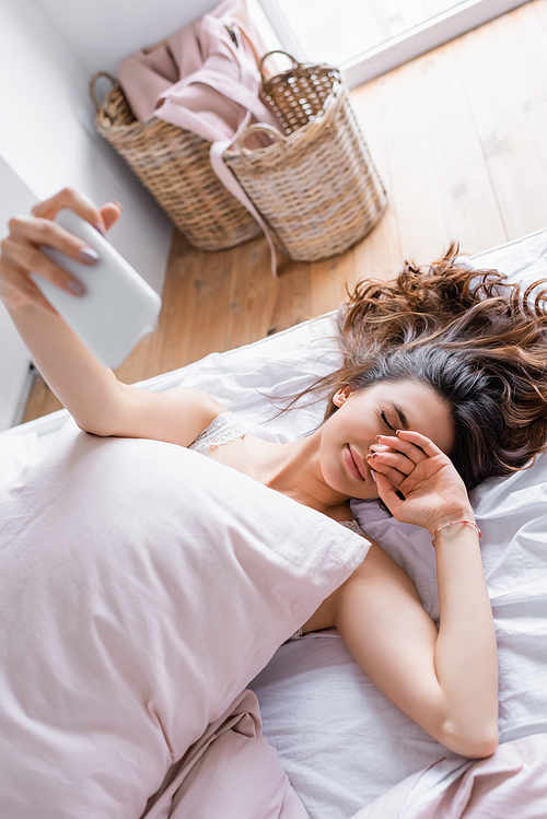 Sleepy woman taking selfie on smartphone on blurred foreground on bed