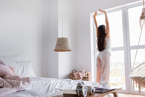 Back view of woman stretching near window in bedroom