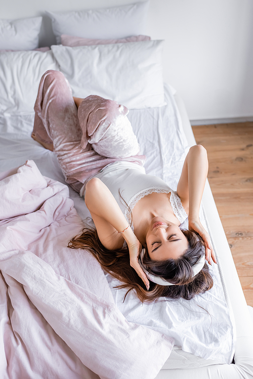 High angle view of woman in pajama and headphones lying on bed during morning