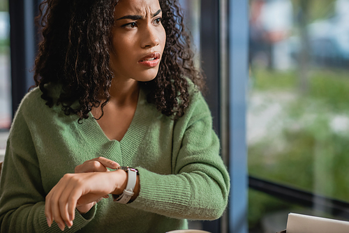 worried african american woman touching watch on wrist while waiting in cafe