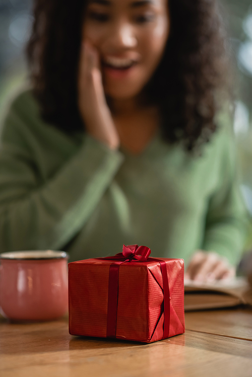 red christmas gift box near amazed african american woman on blurred background