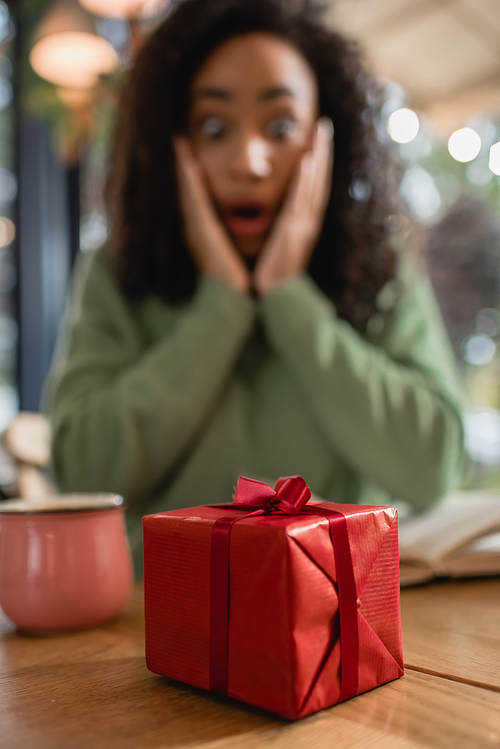 red christmas gift box near shocked african american woman on blurred background