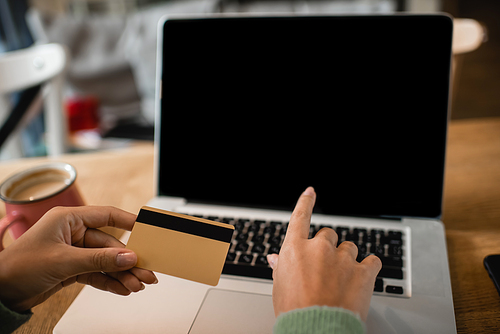 cropped view of young african american woman holding credit card near laptop with blank screen