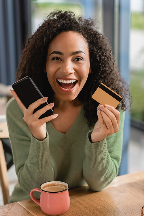 excited african american woman holding smartphone and credit card