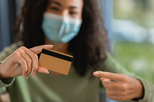 african american woman in medical mask pointing with finger at credit card