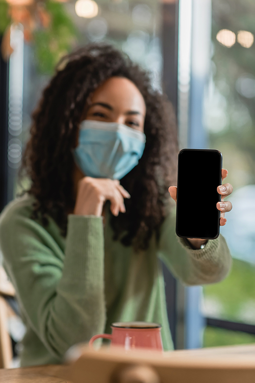 smartphone with blank screen in hand of african american woman in medical mask on blurred background