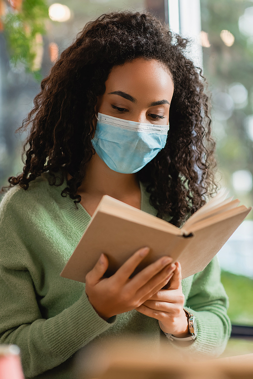 african american woman in medical mask reading book in cafe