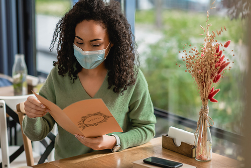 african american woman in medical mask holding menu in cafe