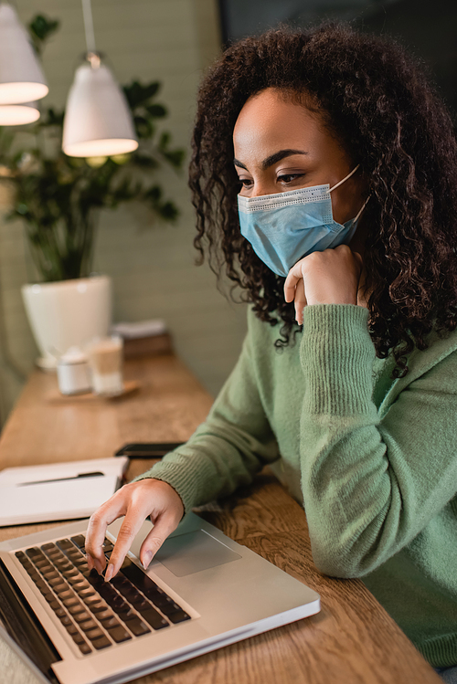 african american woman in medical mask using laptop in cafe