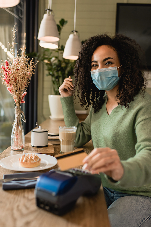 african american woman in medical mask paying for tart and coffee in cafe