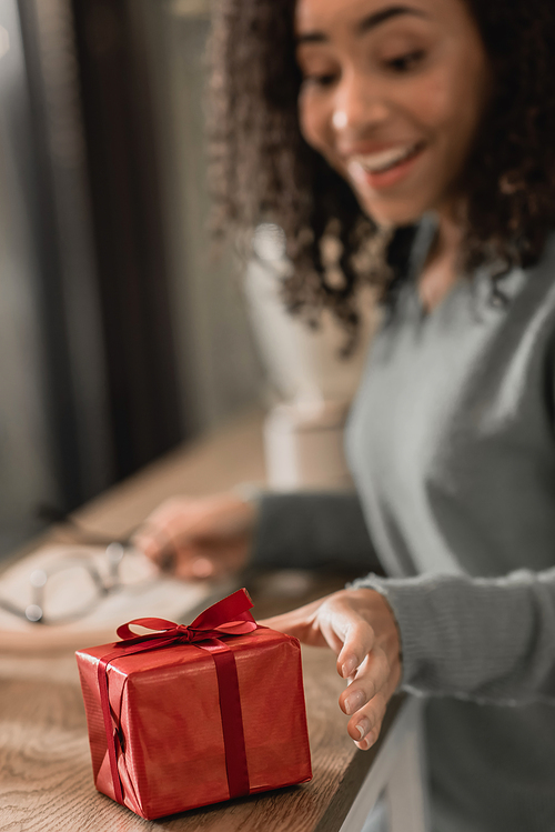 blurred african american woman reaching wrapped christmas present in cafe