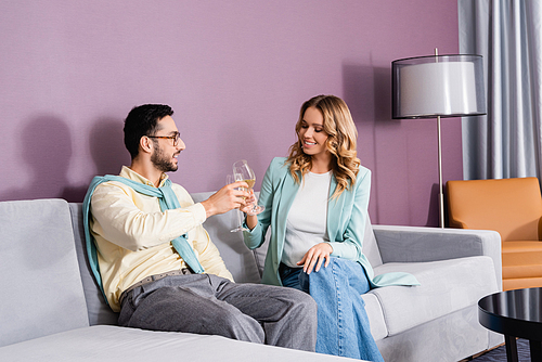 Interracial couple toasting with wine in hotel room