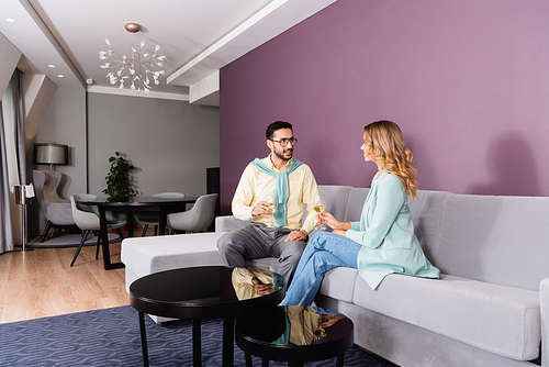 Smiling muslim man looking at girlfriend with glass of wine in hotel