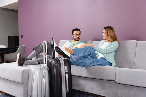 Smiling woman with wine sitting near baggage and muslim boyfriend in hotel room