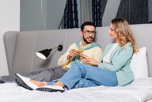 Smiling interracial couple toasting with wine on hotel bed