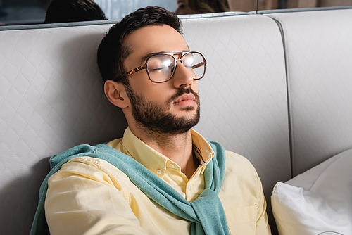 Muslim man in eyeglasses sitting on bed in hotel