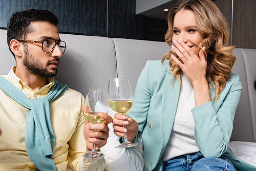 Cheerful woman toasting wine with Muslim boyfriend in hotel
