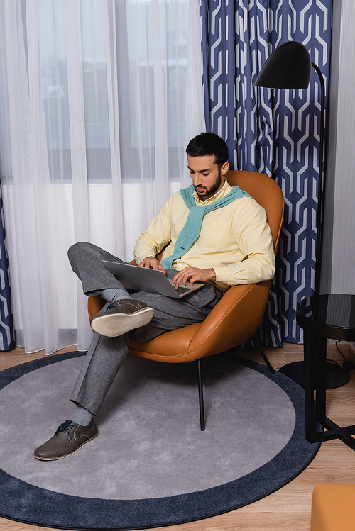 Arabian man using laptop on armchair in modern hotel